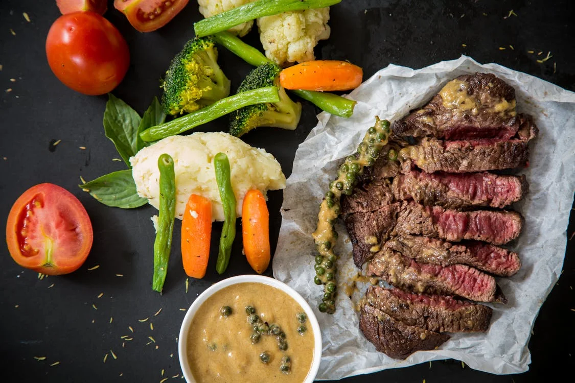 Sliced grilled steak with mashed potatoes, vegetables and pepper sauce